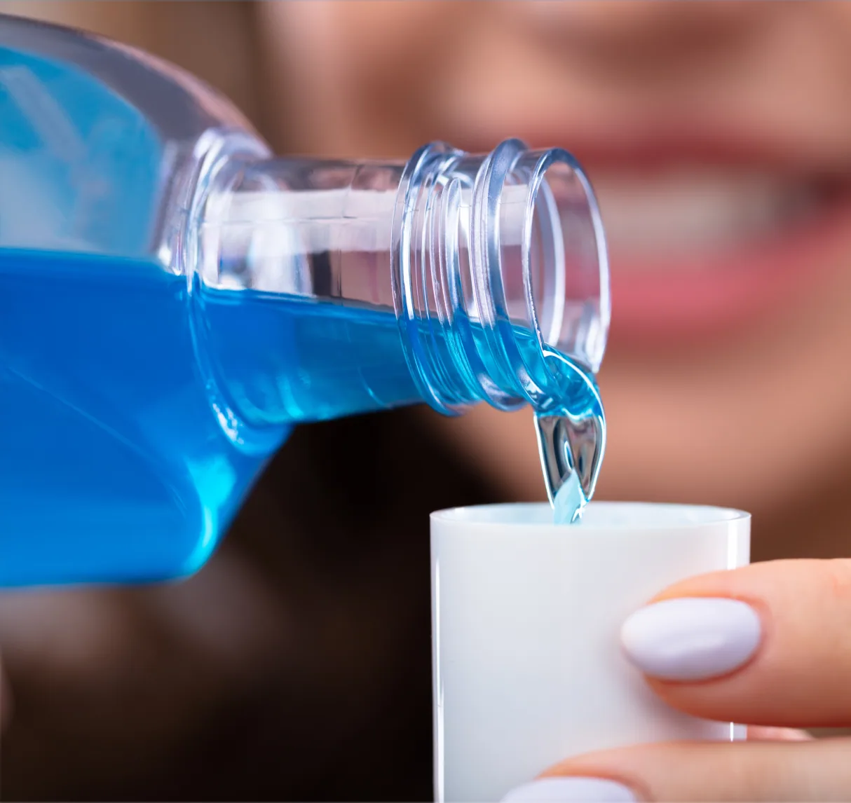 Blue mouthwash being poured from a bottle into a small cup