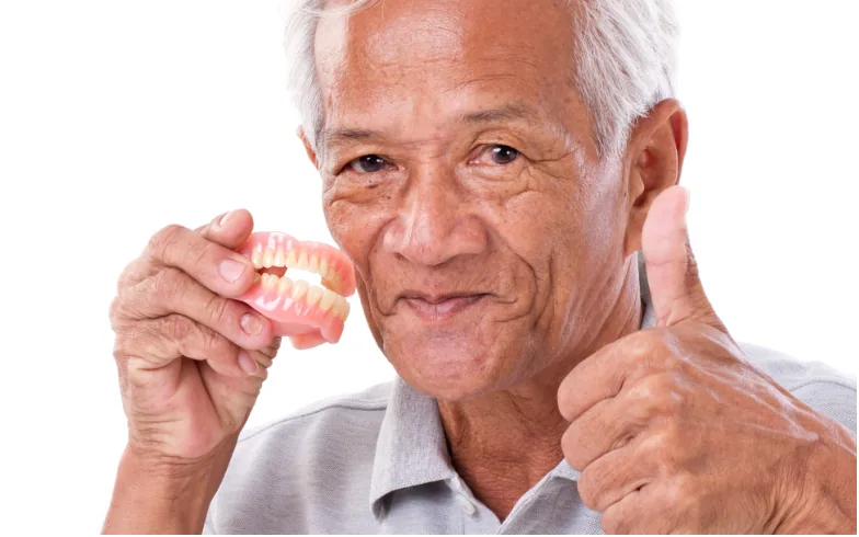 An older man holding his dentures and giving a thumbs up