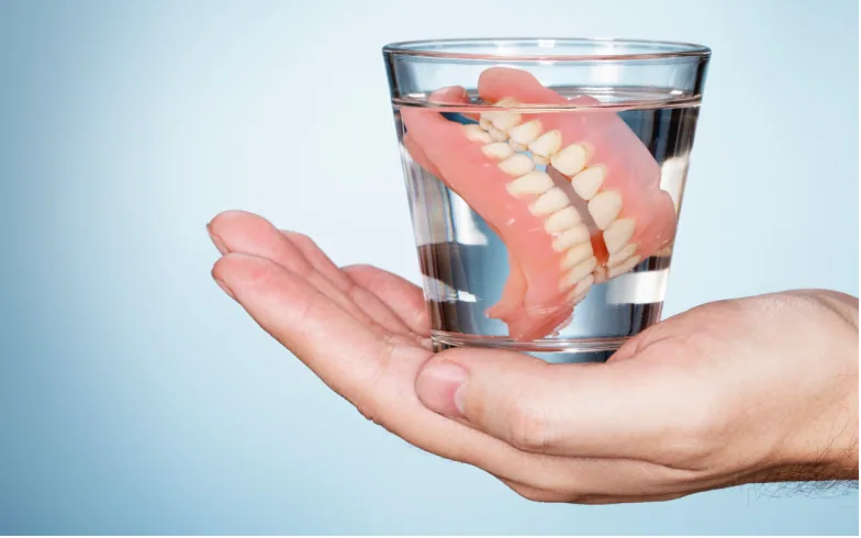Dentures soaking in a glass of water held in a hand